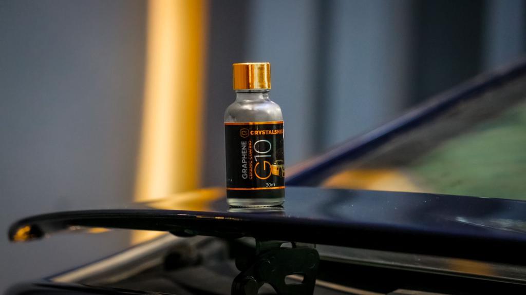 a bottle of graphene ceramic coating placed atop the wing of a black car inside a studio