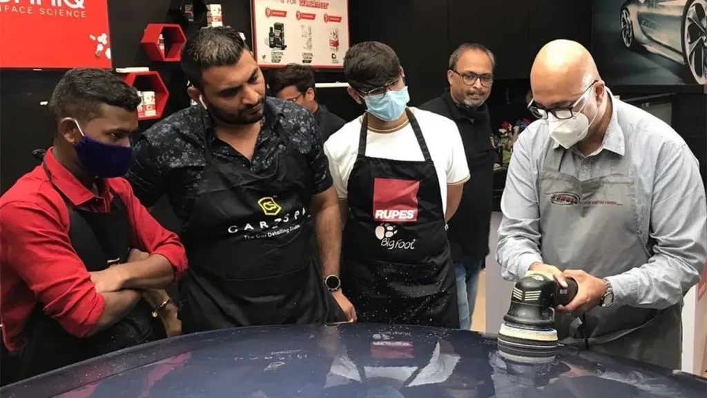 An Indian man conducting a car detailing training session for other detailers around him