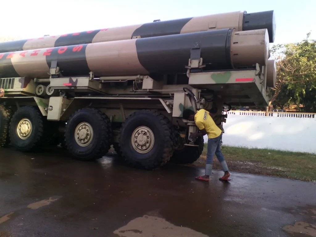 A person in a yellow t-shirt checking a missile placed atop a truck