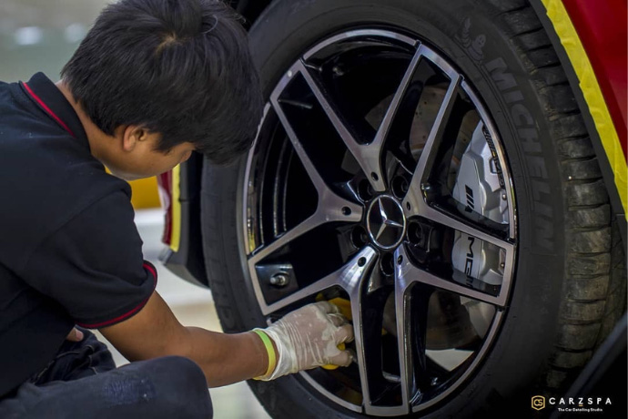 A detailer working on the wheel of a car at a detailing studio