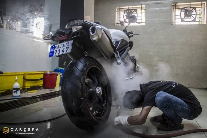 A detailer steam cleans the insides of a silver-grey superbike as part of the detailing job for the vehicle