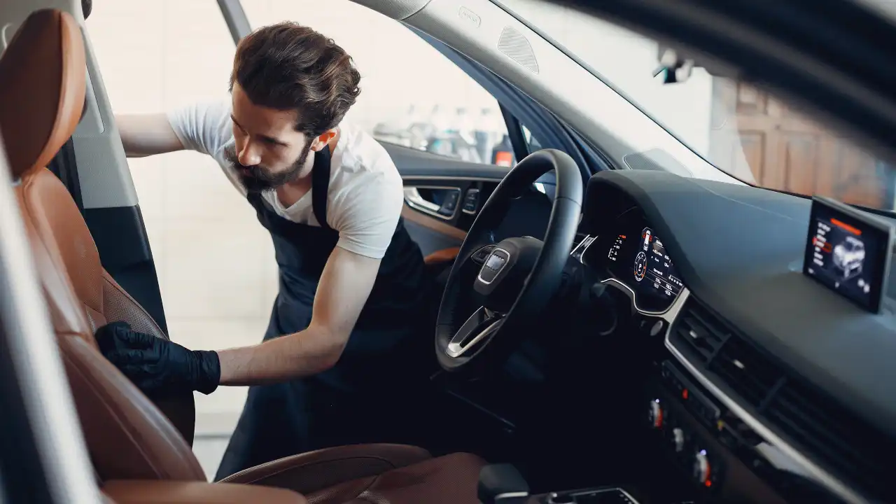 A young automobile detailer working on the interior of the car in a detailing studio