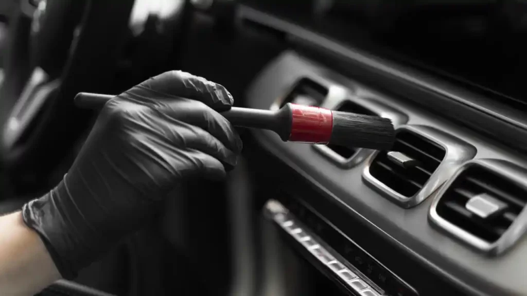 A man using a detailing brush to clean the AC vent of a car