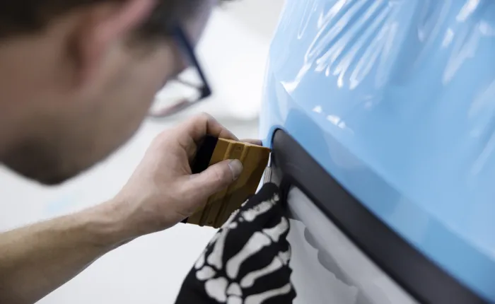 A car detailer applies a blue shade of coloured paint protection film
