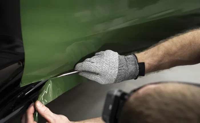 A car detailer cuts a green-coloured paint protection film with great precision