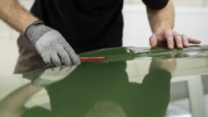 A car detailer applies a paint protection film on a car of another colour in a detailing studio