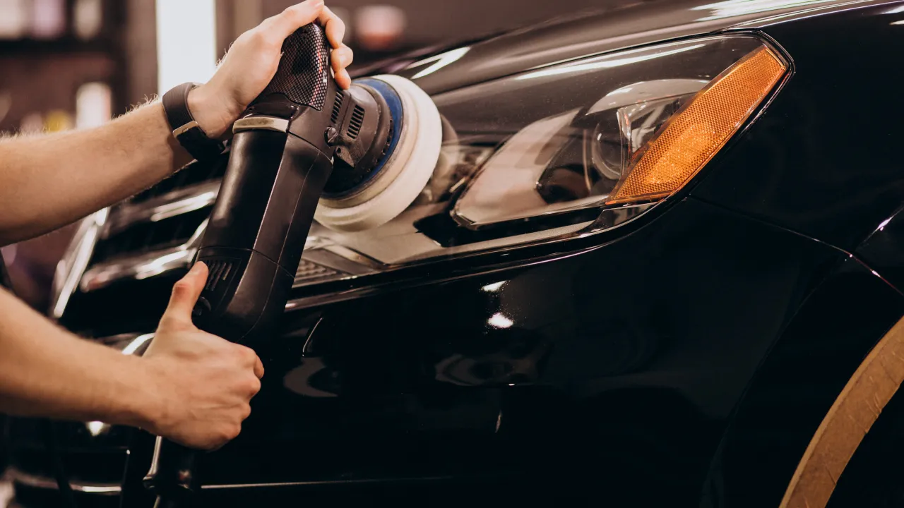 The headlamp of a black car being polished with a polisher by a car detailer