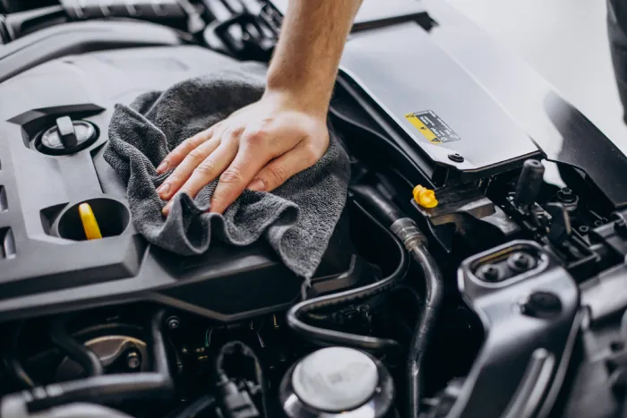 A car detailer works on cleaning the engine of a car