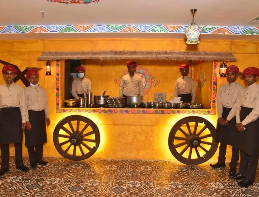 serving staff wearing semi-Rajasthani outfits standing at a serving counter of a restaurant