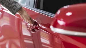 A red coloured brand new car with someone opening the door handle