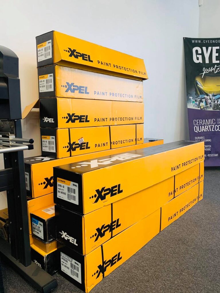 A stack of yellow boxes of Xpel PPF are placed in the corner of a room