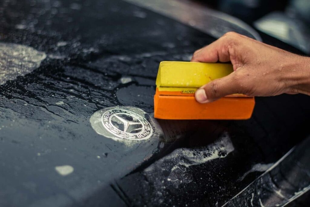 A worker installs a PPF on the door edge of a black SUV with a squeegee