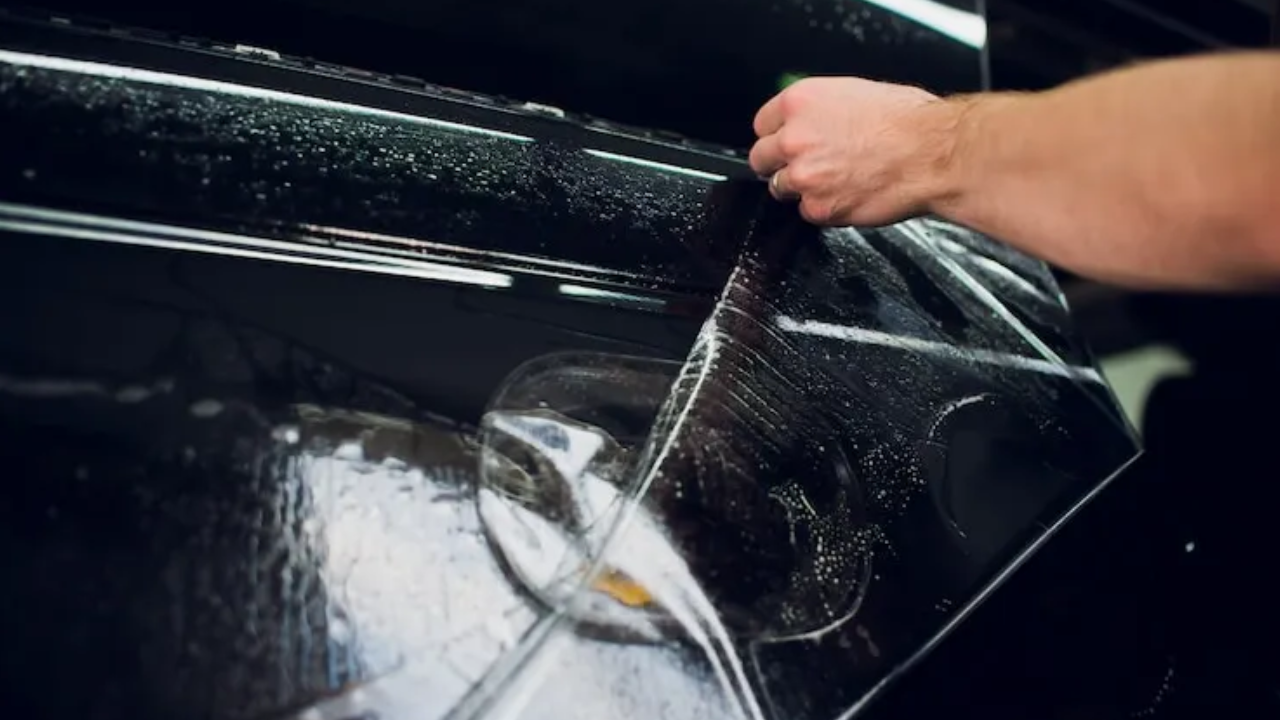 A worker applies a clear PPF on the bonnet of a black Mercedes with the star logo visible through it