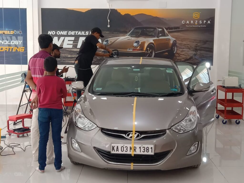 A car detailing worker works on a car, while a father and son look on