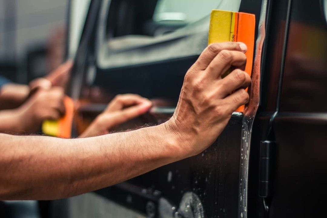 Hand of a worker installing paint protection film on a car with a squeegee