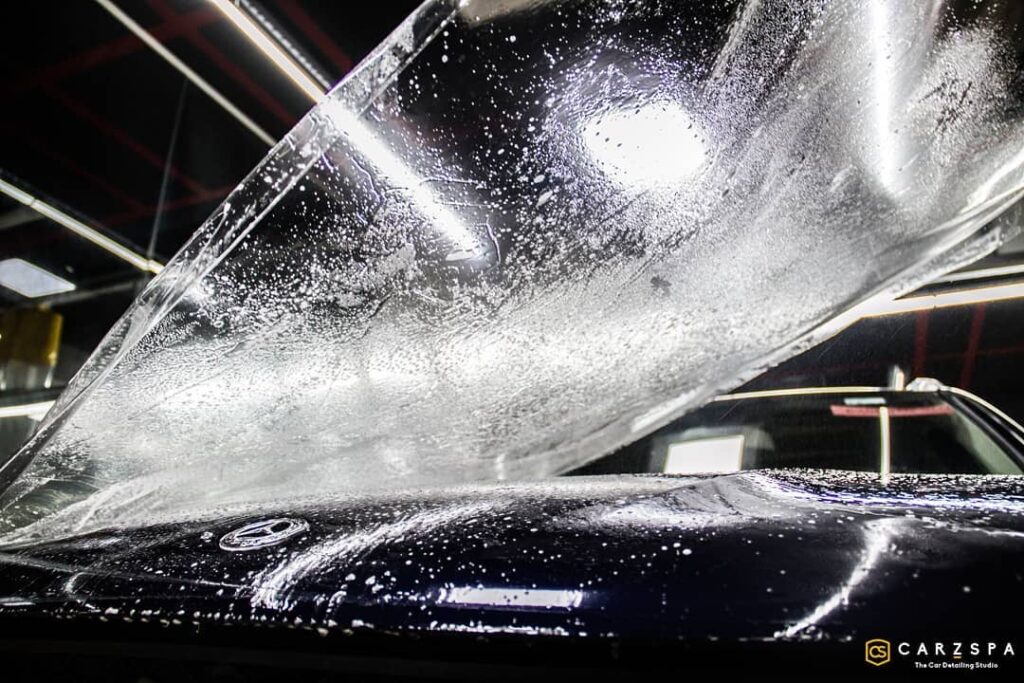 A clear PPF with solution sprayed on it, all set to be placed on the bonnet of a black Mercedes sedan