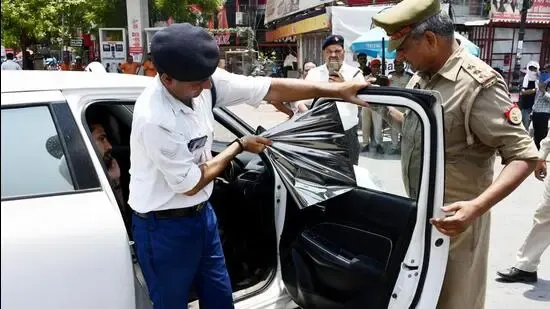 A traffic policeman removes a black car window tint from its side windows on an Indian street