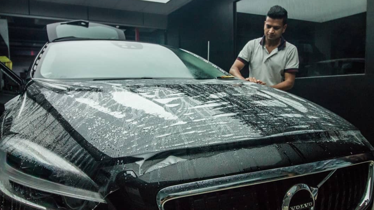 A worker installs a clear paint protection film on a black coloured Volvo sedan.