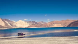 An SUV drives through the banks of a lake with the mountains in the backdrop