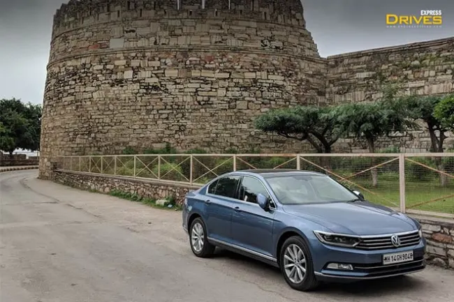A Volkswagen car drives through the lanes of Udaipur by a fort