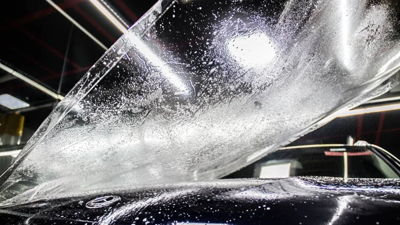 A clear PPF with solution on it about to be installed on the bonnet of a black Mercedes sedan