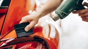 A close-up image of an orange car's curve being installed with a PPF using a squeegee