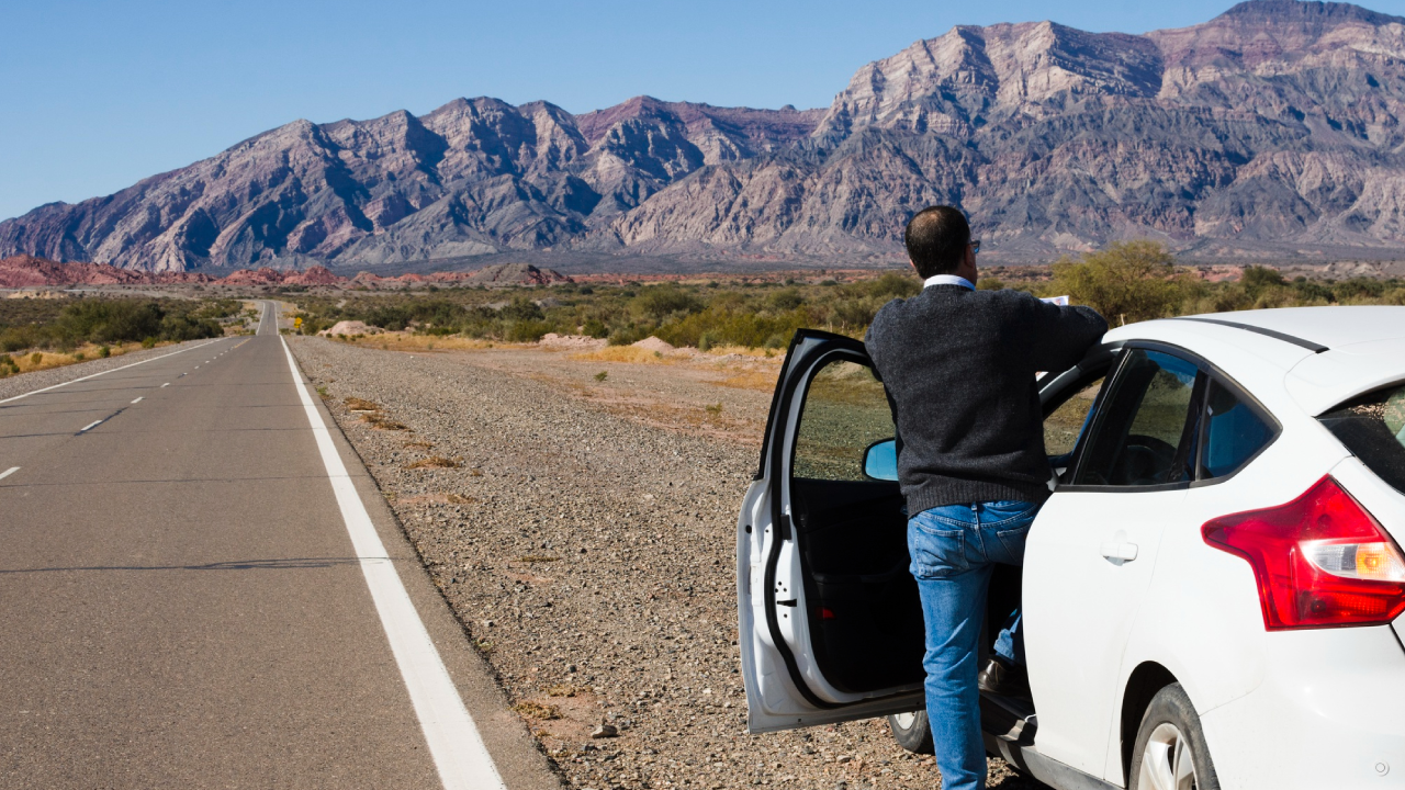 middle aged man enjoys the view of the mountain while standing next to his parked car