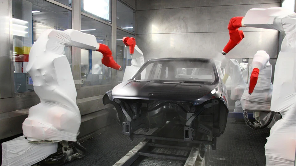 A black coloured car being painted by paint robot inside a paint booth