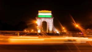 A car zooms past the India Gate, lit in tricolour at night in New Delhi