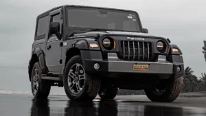 A shiny black Mahindra Thar standing on a dirt road
