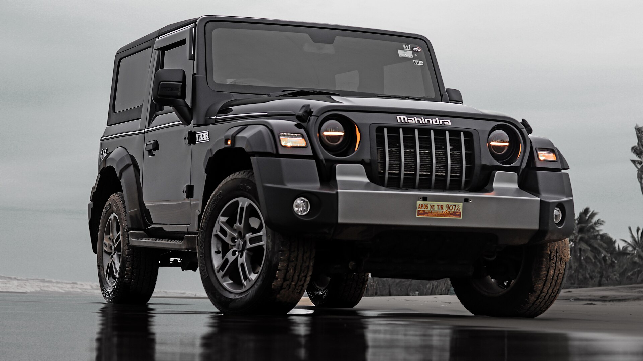 A shiny black Mahindra Thar standing on a dirt road