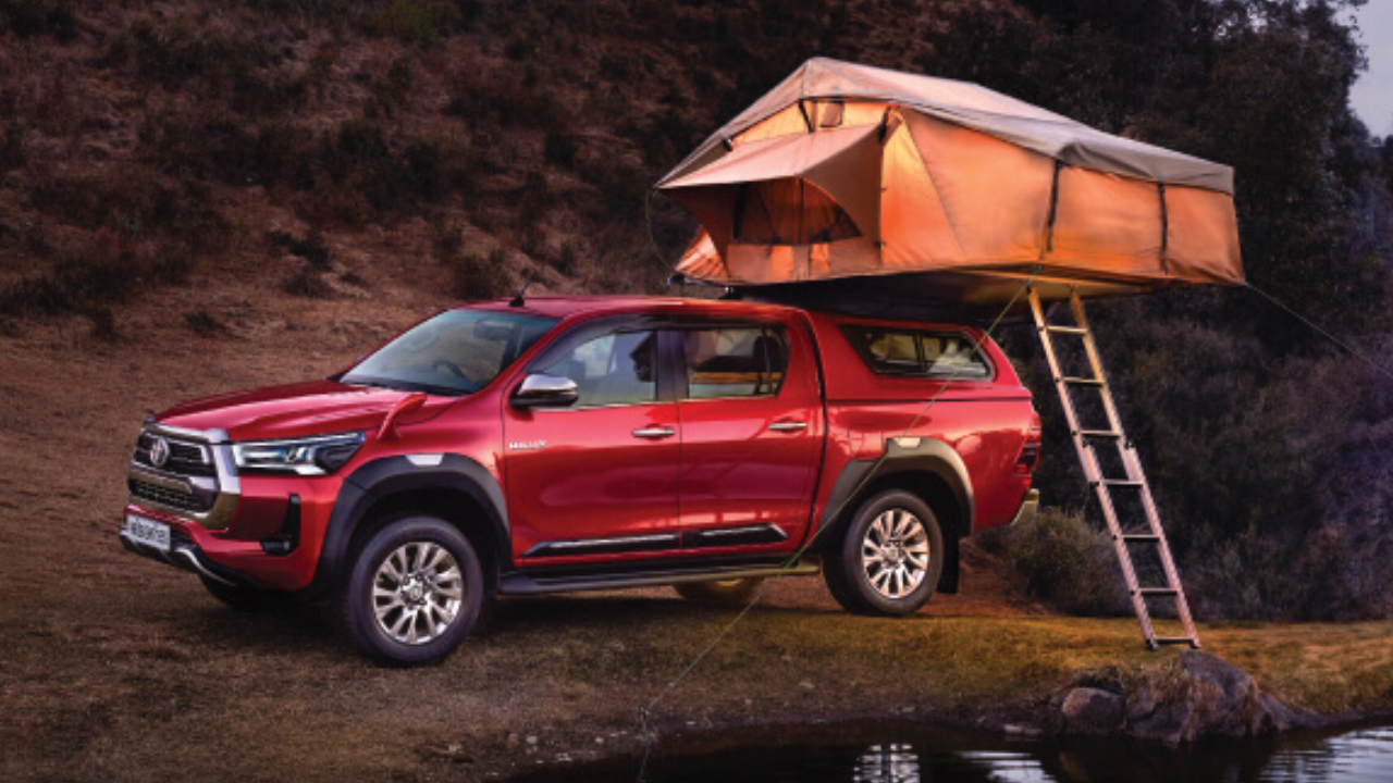 A red Toyota Hilux at an outdoor forest camp with a canopy set up with support of its roof
