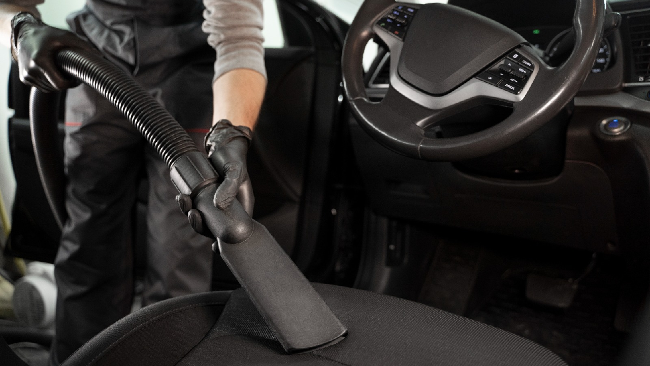 A person vacuums the interior of a car, cleaning the seats and floors thoroughly