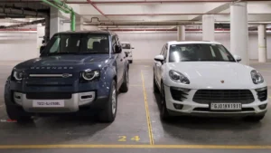 A Land Rover Defender and a white Porsche parked next to each other in a parking garage