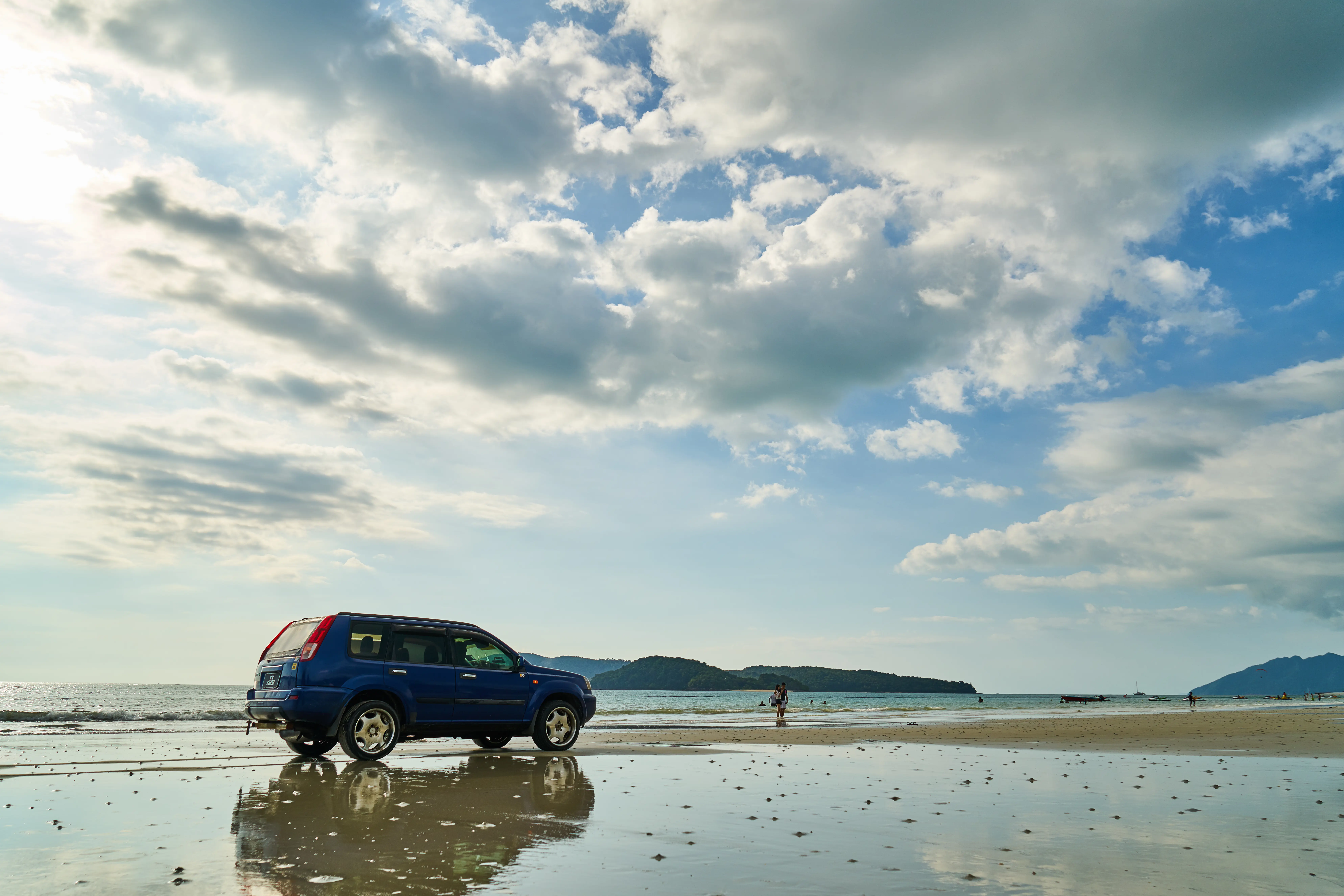 a blue SUV parked in the distance, with its reflection visible on the water.