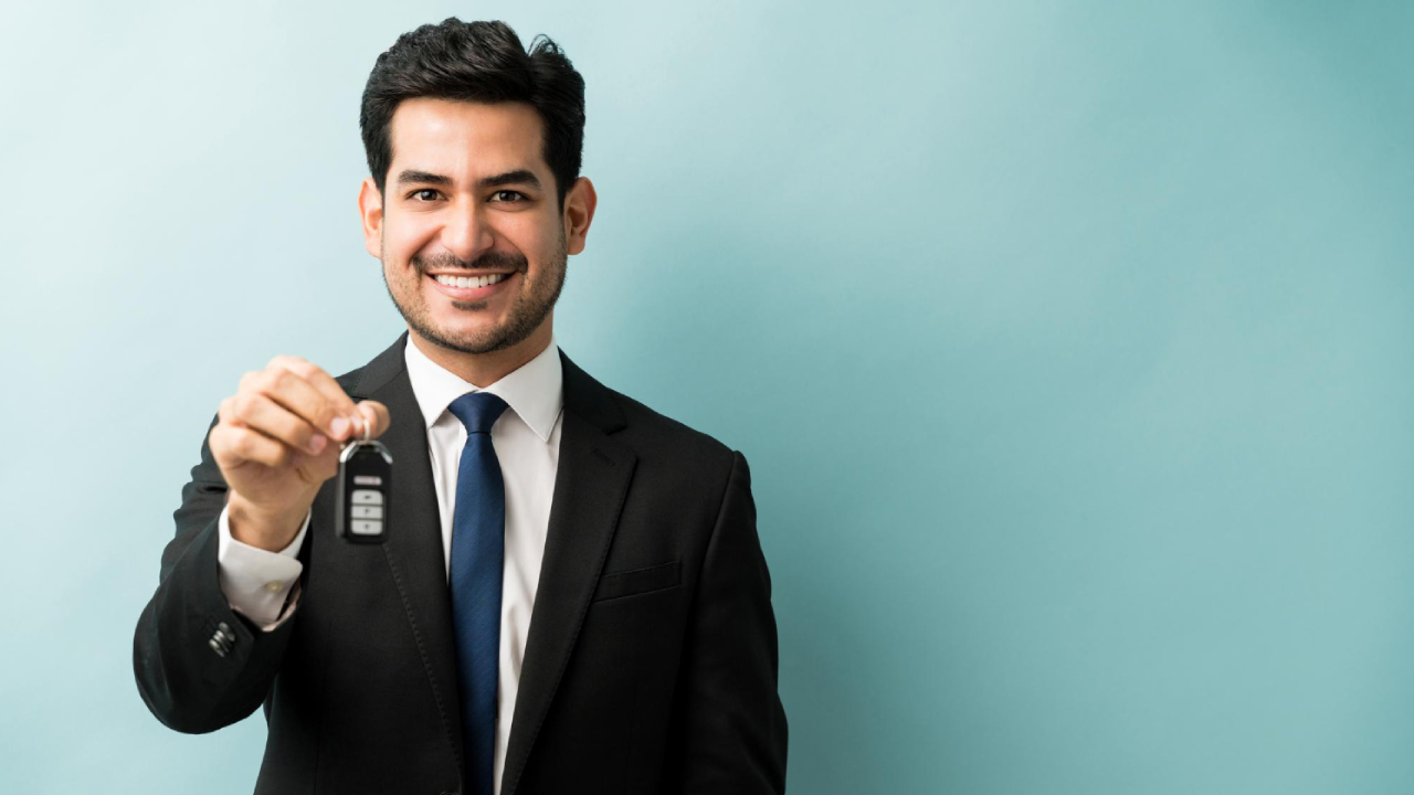 A man in black suit holding up a car key as if offering it to the viewer