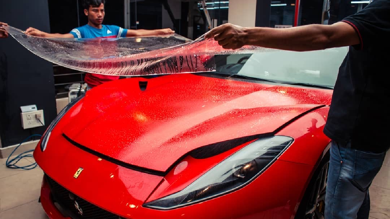 Two workers installing a clear PPF on a luxury car with great care, inside a detailing studio