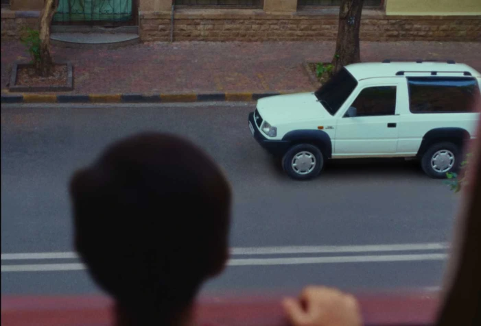 A young kid looks at a 1991 white Tata Sierra on the street from his window
