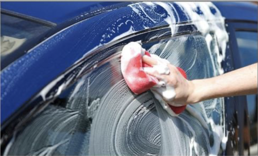 Close-up view of a worker washing a car with a sponge and soapy water