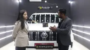 A man and a woman talking to each other in front of an SUV parked inside a workshop