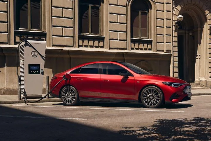 A red Mercedes-Benz CLA Electric plugged into a charging station on the side of a street