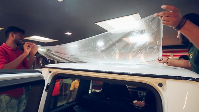 A detailer carefully installing paint protection film on a car's roof