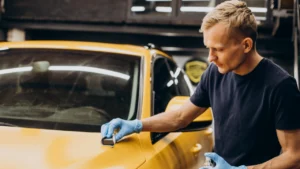 A close-up shot of a worker applying car ceramic coating on a yellow vehicle’s surface.