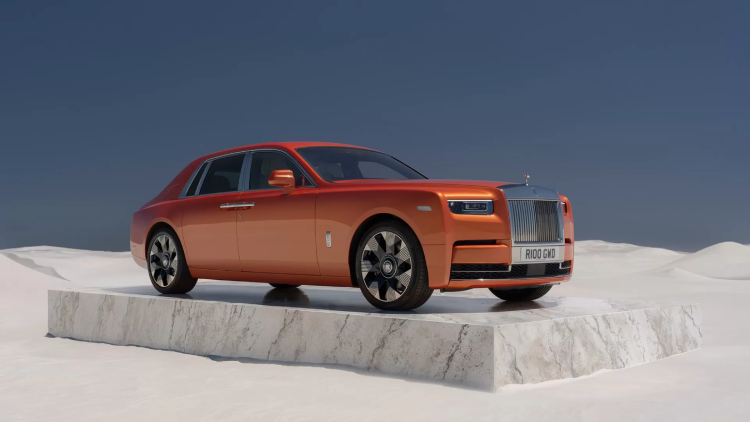An orange Rolls-Royce Phantom VIII Series II stands on a raised platform