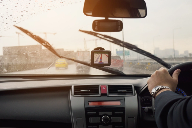 View from inside a car driving in the rain, with windshield wipers moving and a GPS screen on the dashboard.