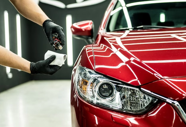 a worker applies car ceramic coating on a red coloured car inside a detailing bay