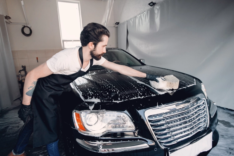 Man washing a black car with a sponge inside a car cleaning garage.