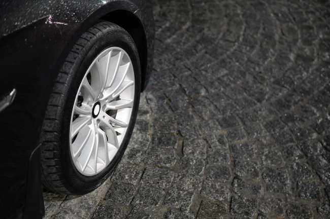 Close-up of a car tyre parked on a wet cobblestone road at night.