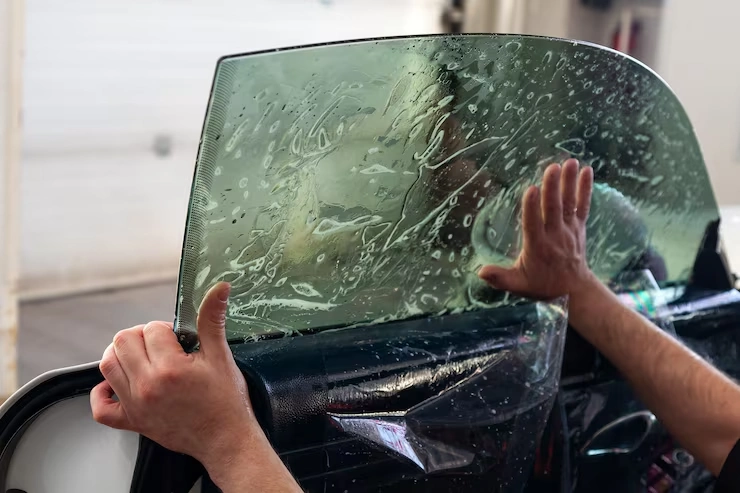 A worker installing a window film on a car’s side glass