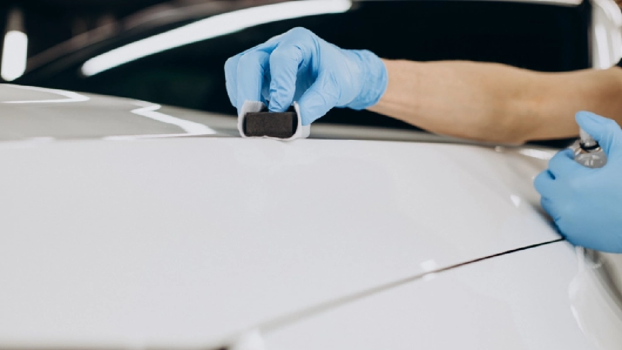 Close-up shot of a white car being applied with ceramic coating treatment at a detailing studio